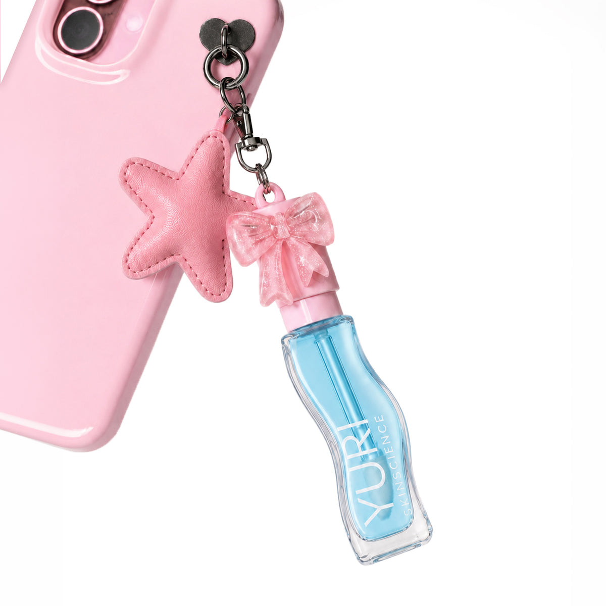 Yuri Skinscience pH reactive lip tint oil clipped to a pink phone case as a charm, with a glitter bow cap and star keyring accessory